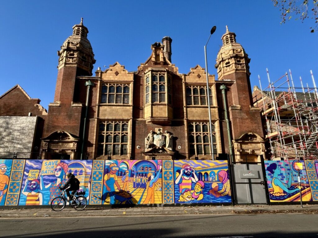 Exterior of Moseley Road Baths with a colourful hoarding depicting swimmers and people from the local community.